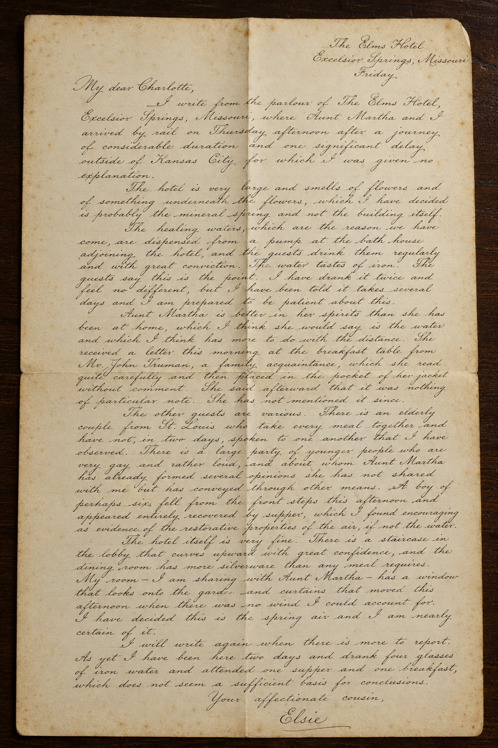 Aged handwritten letter on folded cream paper with The Elms Hotel, Excelsior Springs, Missouri letterhead, written in cursive ink and laid flat on a dark wooden surface