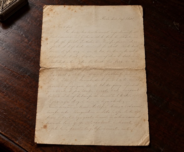 Weathered handwritten letter on aged cream paper resting on a dark mahogany desk.